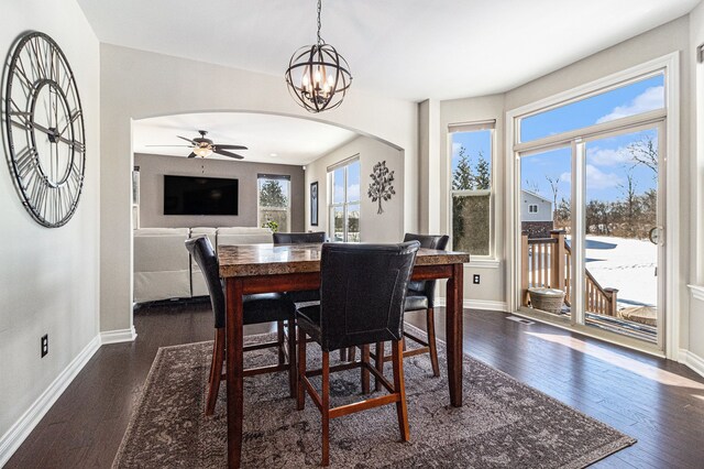 dining room featuring arched walkways, dark wood-type flooring, ceiling fan with notable chandelier, and baseboards