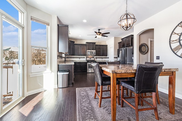 dining space featuring dark wood-style floors, arched walkways, recessed lighting, baseboards, and ceiling fan with notable chandelier