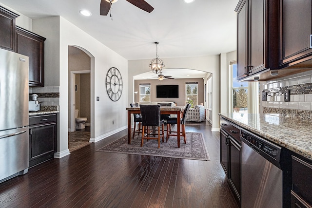 dining space featuring arched walkways, dark wood-style flooring, a ceiling fan, and baseboards