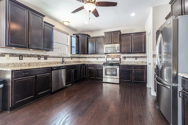 kitchen with appliances with stainless steel finishes, dark wood finished floors, light stone counters, and dark brown cabinetry