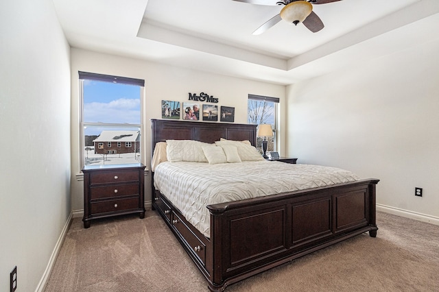 carpeted bedroom featuring a ceiling fan, a raised ceiling, multiple windows, and baseboards