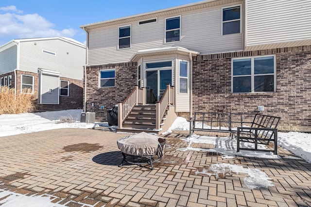 snow covered property with a fire pit, a patio, brick siding, and entry steps