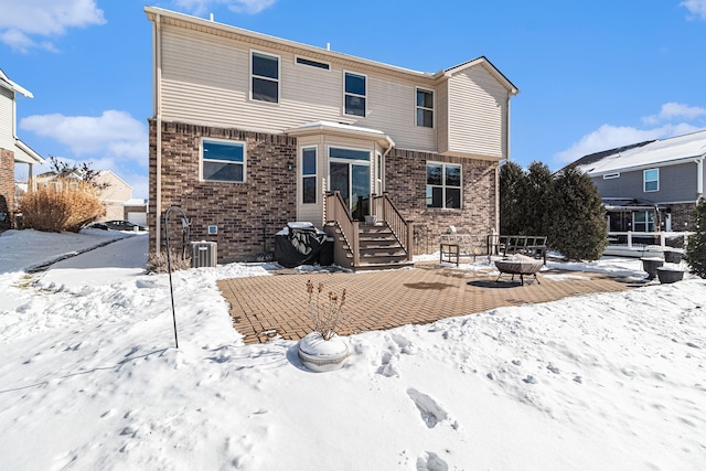 snow covered back of property featuring an outdoor fire pit and brick siding