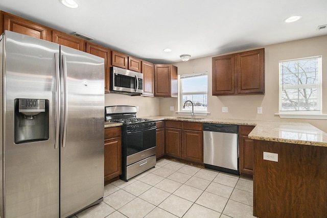 kitchen with sink, light tile patterned flooring, stainless steel appliances, kitchen peninsula, and light stone countertops