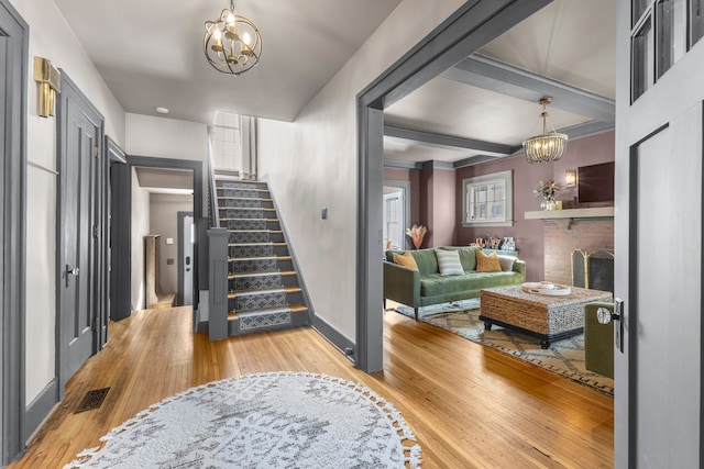 entryway with a chandelier, stairway, light wood-type flooring, and a brick fireplace