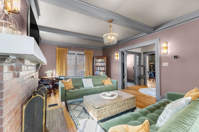 living area with a notable chandelier, wood finished floors, visible vents, a brick fireplace, and beamed ceiling