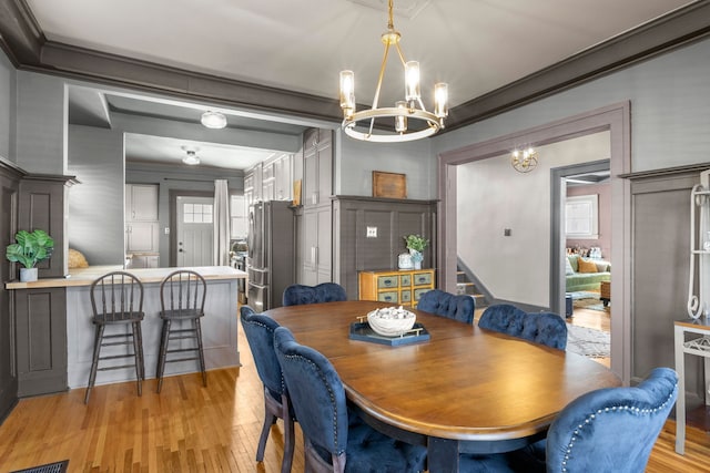 dining area with crown molding, light wood finished floors, stairs, and an inviting chandelier