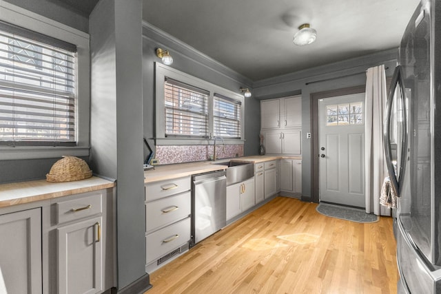 kitchen featuring appliances with stainless steel finishes, light countertops, a sink, and gray cabinetry