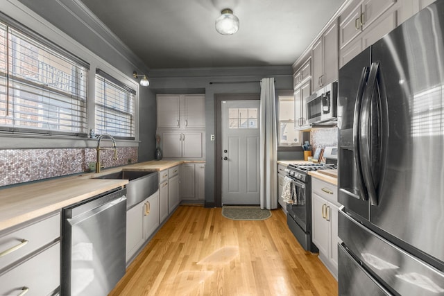 kitchen with gray cabinets, appliances with stainless steel finishes, light wood-style floors, ornamental molding, and a sink