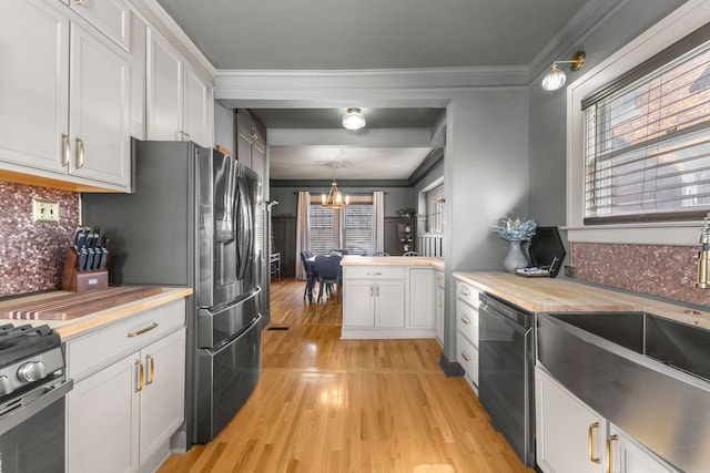 kitchen featuring a notable chandelier, white cabinetry, ornamental molding, appliances with stainless steel finishes, and pendant lighting