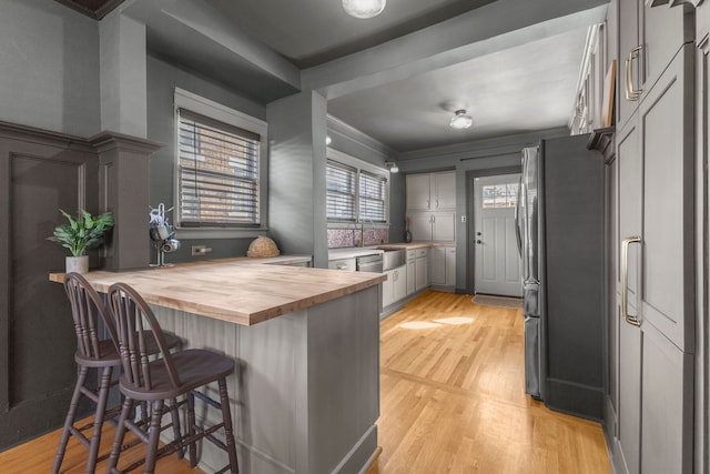 kitchen with light wood finished floors, a kitchen breakfast bar, freestanding refrigerator, gray cabinetry, and wooden counters