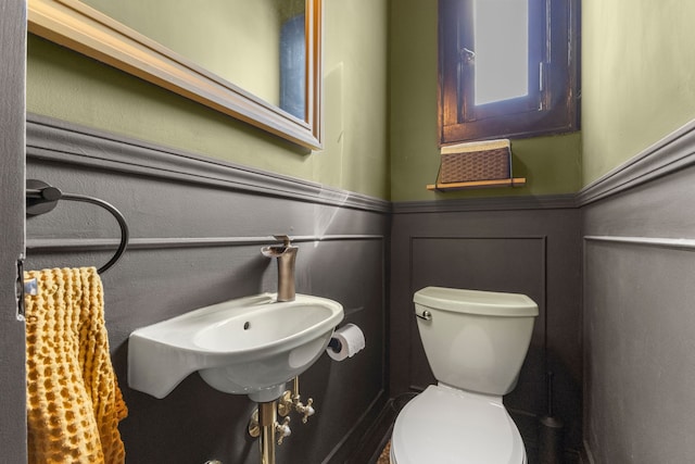 bathroom featuring wainscoting, a decorative wall, and toilet