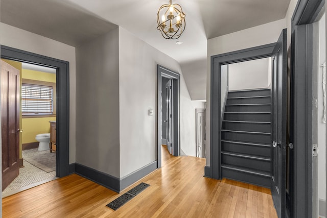 hallway featuring visible vents, stairway, an inviting chandelier, wood finished floors, and baseboards