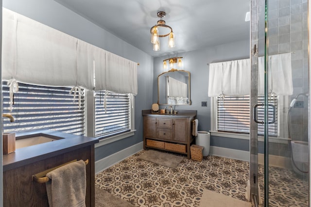 bathroom with a stall shower, two vanities, a sink, and baseboards