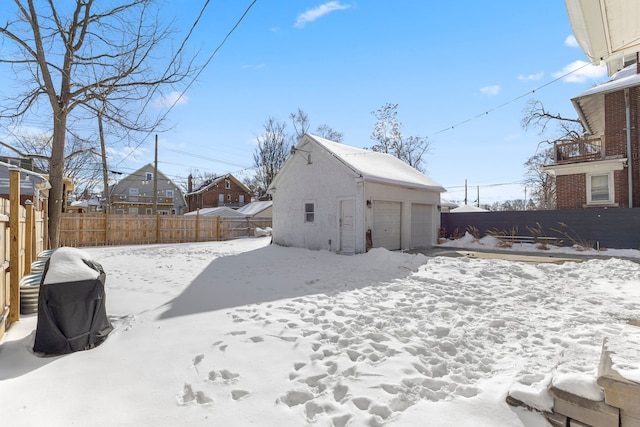 snowy yard featuring a garage, an outdoor structure, and fence