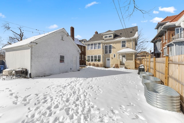 snow covered rear of property with a chimney and fence