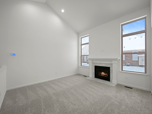 unfurnished living room featuring high vaulted ceiling, light colored carpet, and a premium fireplace