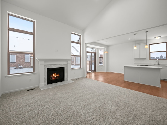 unfurnished living room with high vaulted ceiling, a high end fireplace, light colored carpet, and sink