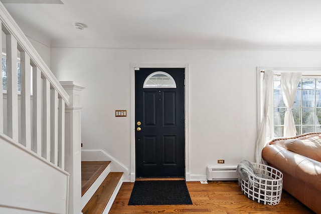 foyer entrance featuring a baseboard heating unit, wood finished floors, baseboards, and stairs