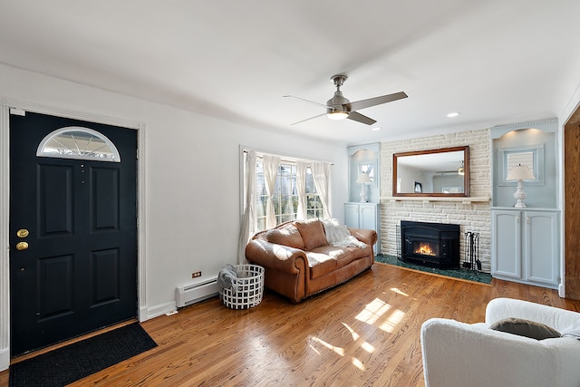 living room featuring ceiling fan, light wood-style flooring, a fireplace, baseboards, and baseboard heating