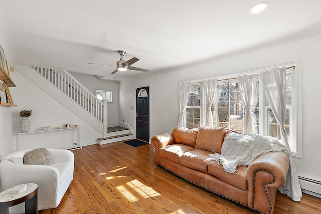 living room with a ceiling fan, stairs, a baseboard heating unit, and wood finished floors