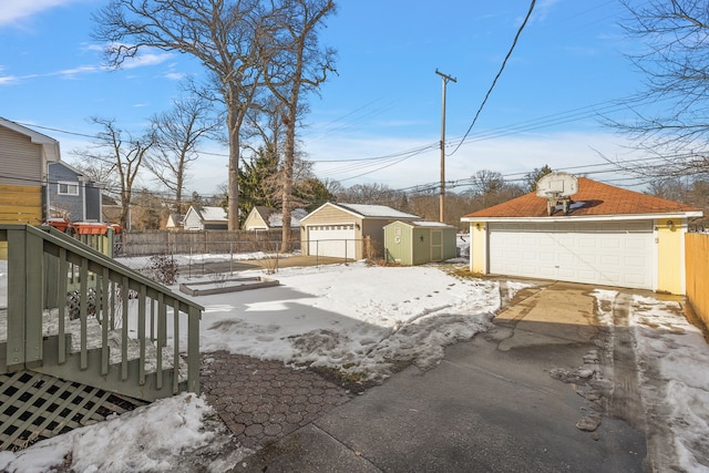 snowy yard featuring a shed, an outdoor structure, fence, and a detached garage