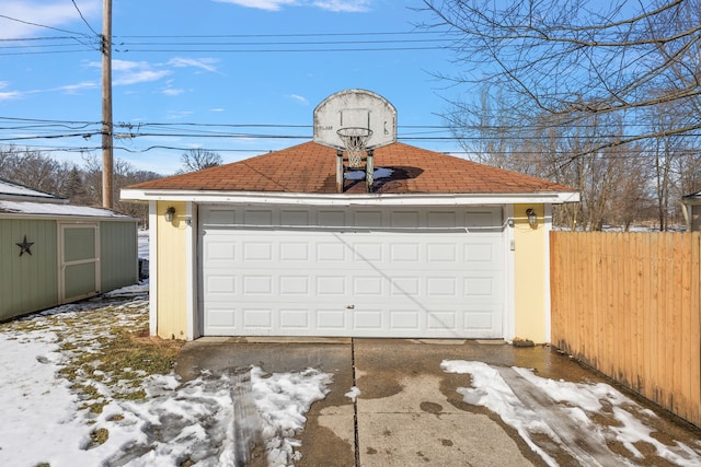 snow covered garage featuring a garage and fence