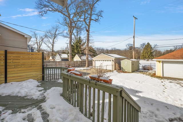 yard covered in snow featuring a garage, an outbuilding, fence, and a storage shed