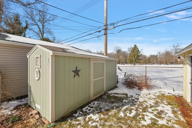 snow covered structure with an outbuilding, a storage unit, and fence