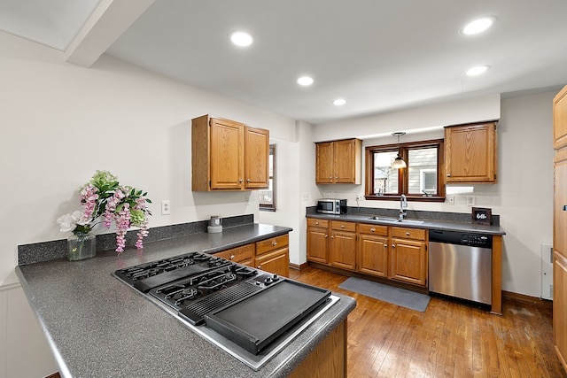 kitchen with appliances with stainless steel finishes, dark countertops, brown cabinets, and a sink