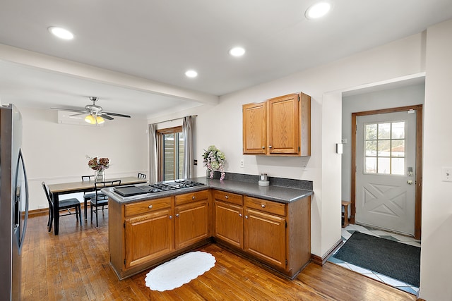 kitchen featuring dark countertops, appliances with stainless steel finishes, brown cabinetry, wood finished floors, and a peninsula