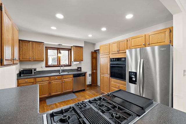 kitchen with light wood finished floors, dark countertops, appliances with stainless steel finishes, a sink, and recessed lighting