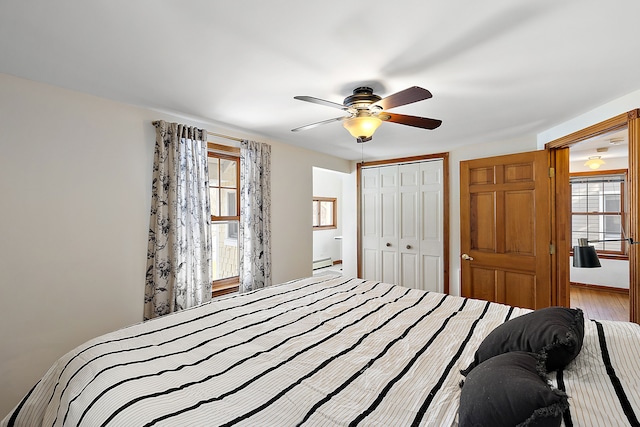 bedroom with light wood-type flooring, multiple windows, a baseboard heating unit, and a closet