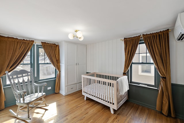 bedroom featuring light wood-style floors, baseboards, and a wall mounted AC