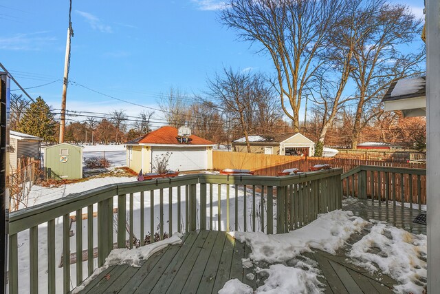 snow covered deck with a fenced backyard, an outdoor structure, and a shed