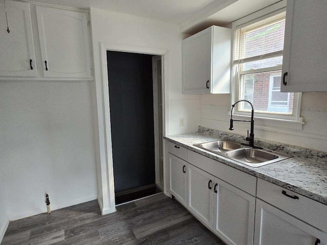 kitchen with a sink, white cabinetry, baseboards, light countertops, and dark wood finished floors