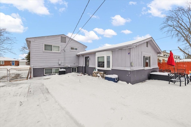 snow covered house featuring cooling unit and fence