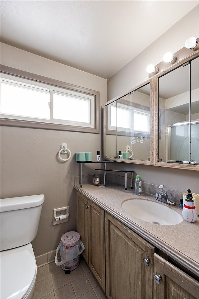 bathroom featuring a shower with shower door, toilet, vanity, baseboards, and tile patterned floors