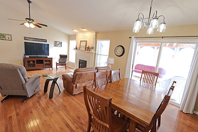 dining area with a fireplace, light hardwood / wood-style floors, vaulted ceiling, and ceiling fan with notable chandelier