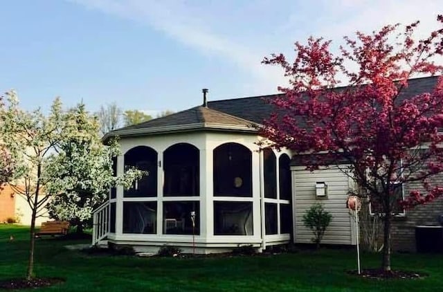 back house at dusk featuring a sunroom and a lawn