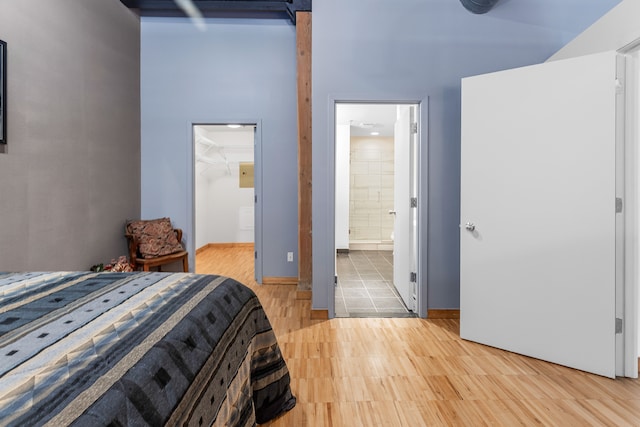 bedroom featuring a walk in closet, ensuite bath, light wood-style flooring, and baseboards