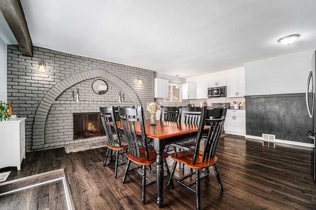 dining area featuring visible vents, brick wall, dark wood finished floors, beamed ceiling, and a fireplace