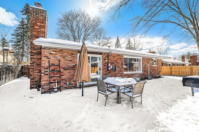 snow covered property with fence, brick siding, and a chimney