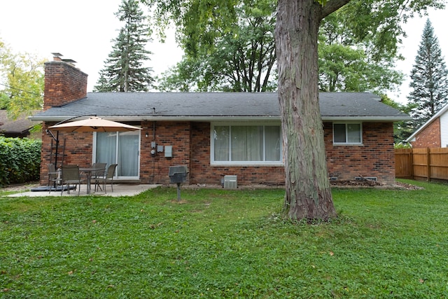 rear view of property with brick siding, a chimney, a yard, and fence