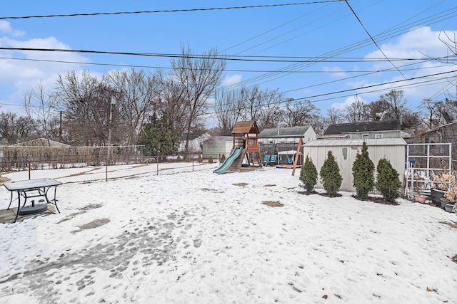 snowy yard with a playground and a storage shed