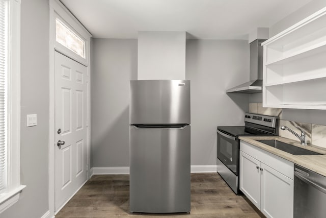 kitchen with hardwood / wood-style floors, appliances with stainless steel finishes, sink, white cabinetry, and wall chimney exhaust hood