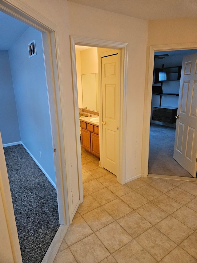 corridor featuring light tile patterned floors, baseboards, visible vents, and light colored carpet