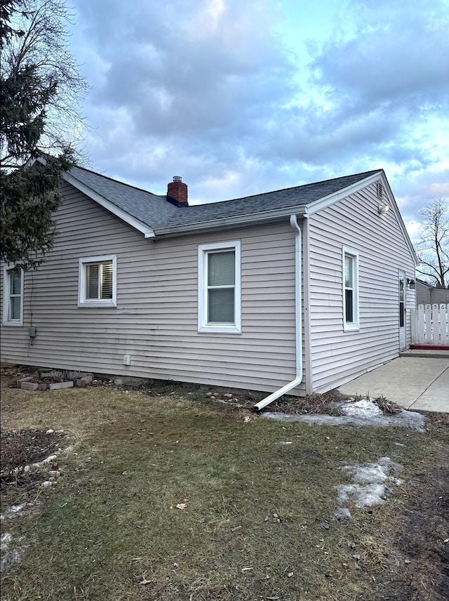 view of home's exterior with a yard, a chimney, and roof with shingles