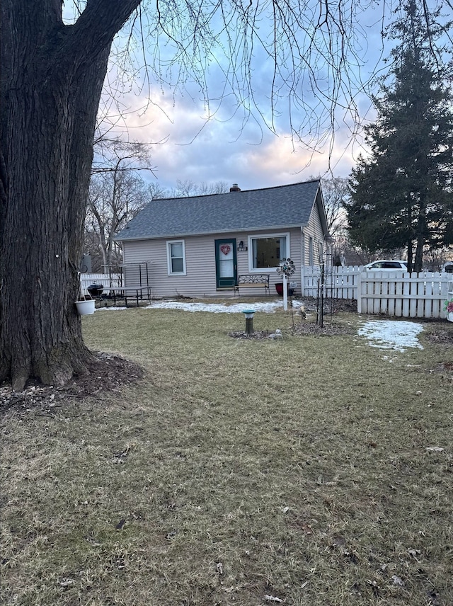 view of front of house with a front lawn, roof with shingles, a chimney, and fence