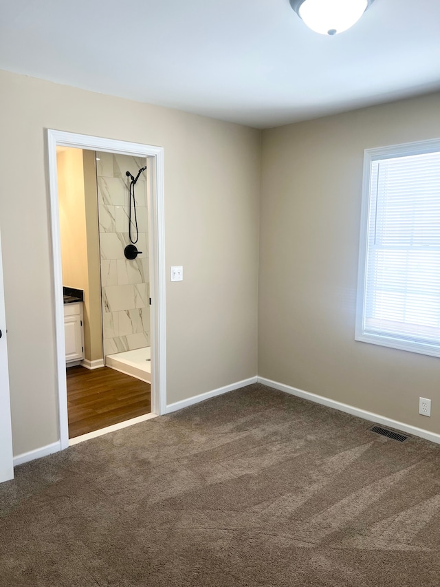 unfurnished bedroom featuring ensuite bathroom and dark carpet